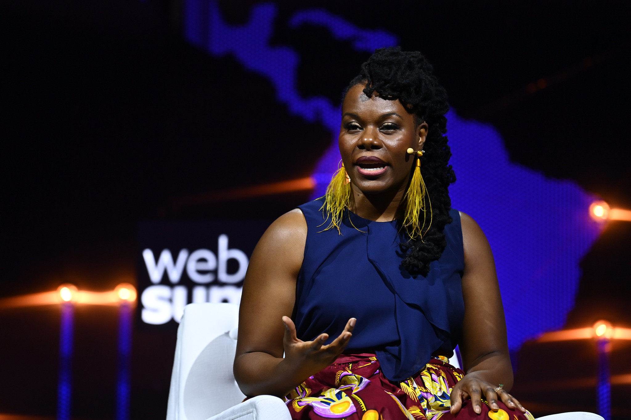 Photograph of The Solutions project CEO Gloria Walton speaking on the Planet Tech Stage at Web Summit. Gloria is gesturing with hands and sitting on a chair.
